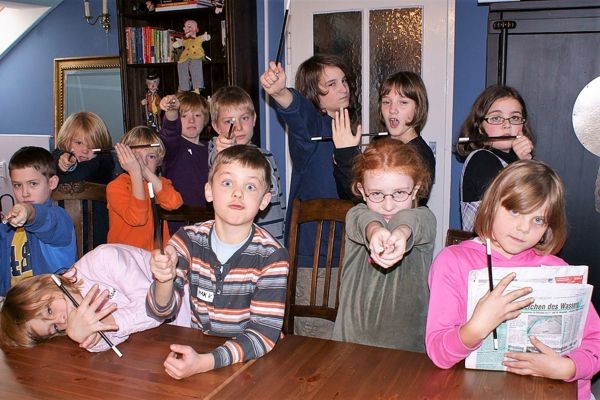 Kinder lernen Zaubertricks mit Zeitungen und Karten am Tisch